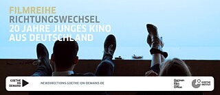 Vor dem Hintergrund einer blau erleuchteten Leinwand sind zwei paar Füße von Menschen zu sehen, die sie auf die Stuhllehnen vor sich gelegt haben.