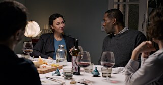 Monika (Ursula Strauss) und Joseph (Passi Balende) sitzen mit Freunden an einem Tisch