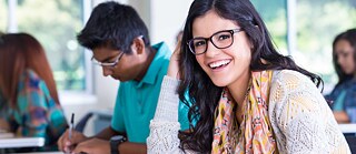 jovem aluna sentada em mesa de estudos sorri para a câmera