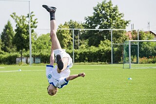 Ein Junge auf dem Fußballfeld macht einen Salto.