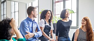 Eine Gruppe junger Leute bei einem Meeting. Sie unterhalten sich und lachen fröhlich. 