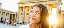 A young smiling woman stands in front of the Brandenburg Tor in Berlin.