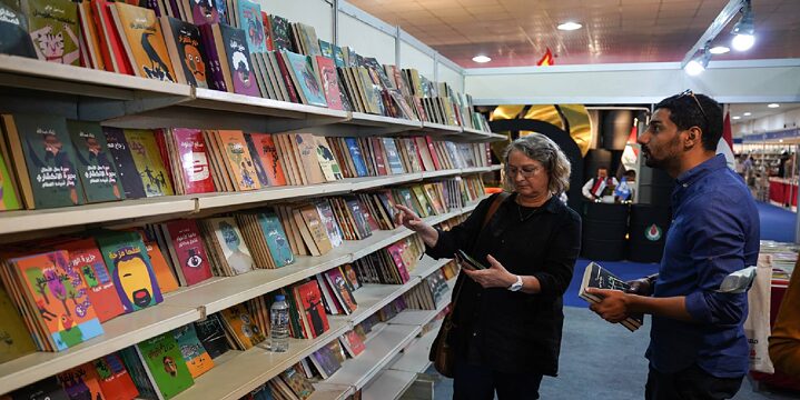 Larissa Bender steht vor einem Bücherregal auf der Buchmesse und unterhält sich mit einem Nutzer