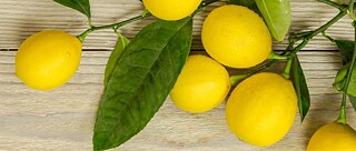 Six lemons with their twigs and leaves are placed on a wooden surface.