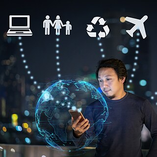 Mann mit Handy vor einem Hologramm einer Weltkugel im Hintergrund befinden sich verschiedene Symbole wie ein Flugzeug oder ein Computer.