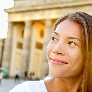 Eine junge lächelnde Frau steht vor dem Brandenburger Tor.