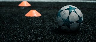 Fußball und orangene Kegel liegen im Gras