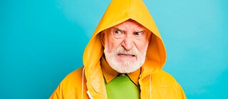 An older man in a yellow rain jacket with an annoyed expression on his face