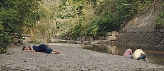 Une femme couchée sur le bord d'une fleuve. « Concrete Valley » arrêt sur l'image.