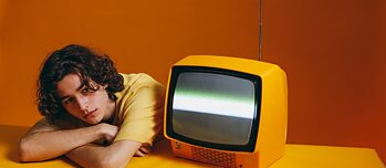 Young man sits next to an orange television
