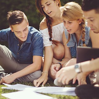 Teenagers studying together in the park in front of spread-out materials.