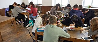 Žáci sedí u stolů a píší.