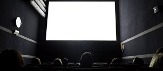 Publikum in einem Kinosaal – Blick auf die strahlend weiß beleuchtete Leinwand