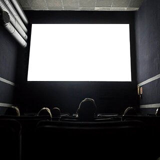 Publikum in einem Kinosaal – Blick auf die strahlend weiß beleuchtete Leinwand