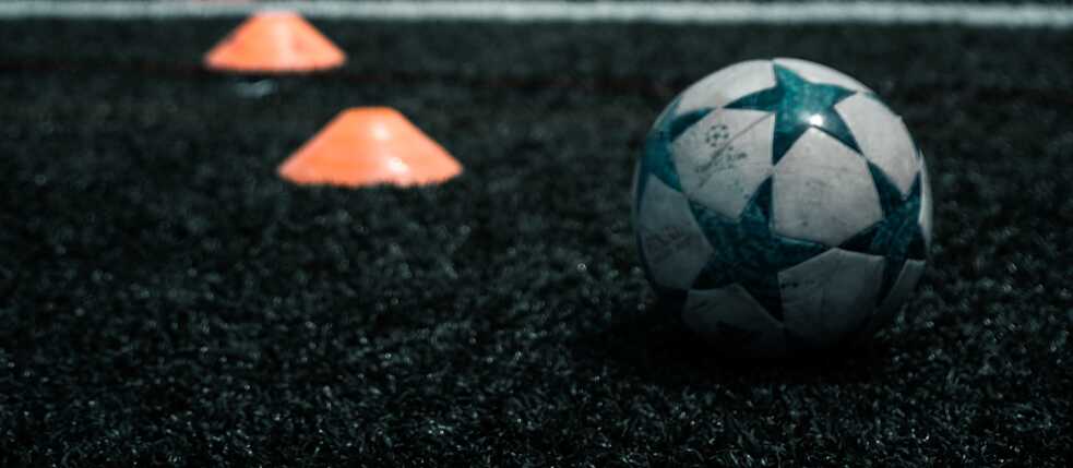 Fußball und orangene Kegel liegen im Gras