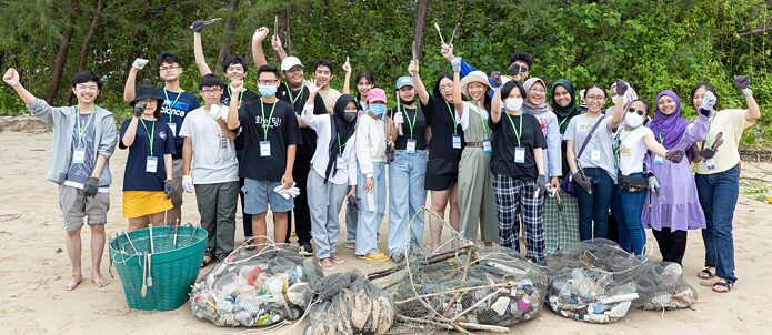 A group of young people stands on the beach cheering with nets full of garbage.