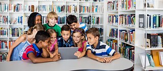Kinder in der Bibliothek schauen gemeinsam auf einen Laptop