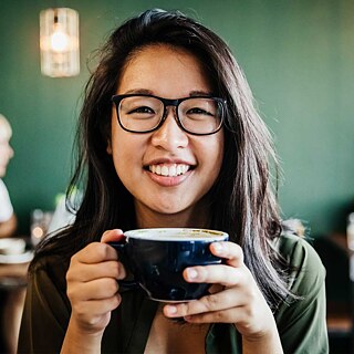 junges Mädchen hält Kaffeetasse und lächelt in die Kamera