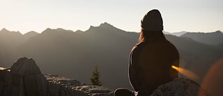 Woman is sitting on a mountain and is looking into valley.