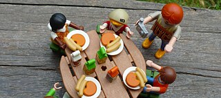 Spielfiguren sitzen am Tisch und essen gemeinsam