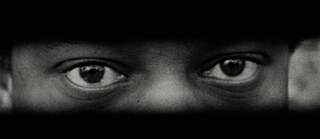 Ein junger Schwarzer blickt durch einen Spalt so dass nur die Augen sichtbar sind