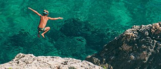 Ein junge springt vom Felsen in ein türkisblaues Meer 