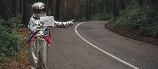 Spaceman hitchhiking to Mars, standing on road in forest