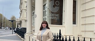 Sarah steht vor dem Institut mit cremefarbenem Pullover