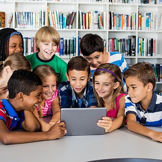 Kinder in der Bibliothek schauen gemeinsam auf einen Laptop