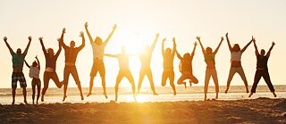 Люди на пляжі стрибають разом із піднятими вгору руками © © GettyImages Літня академія