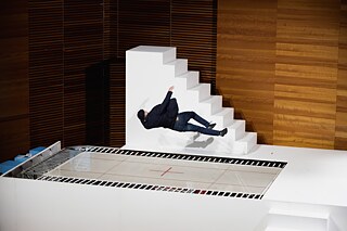 The artist Yoann Bourgeois drops into a trampoline from a white staircase.