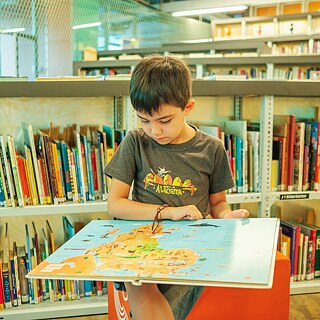 Una niña está sentada en la biblioteca y mira un libro