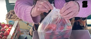 Руки упаковывают клубнику в пластиковый пакет на рынке