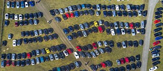 Parkplatz mit vielen Autos auf einer Wiese, von oben gesehen