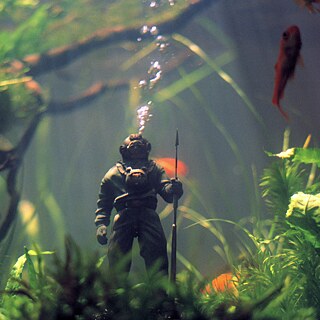 Σκηνή από την ταινία «Undine»: Μια φιγούρα δύτη σε ενυδρείο είναι περιτριγυρισμένη από ψάρια και φυτά. Από τη φιγούρα αναδύονται φυσαλίδες αέρα.