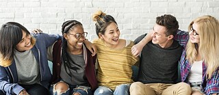  Vários jovens estudantes sentam-se de braços dados um ao lado do outro em um sofá e sorriem um para o outro.