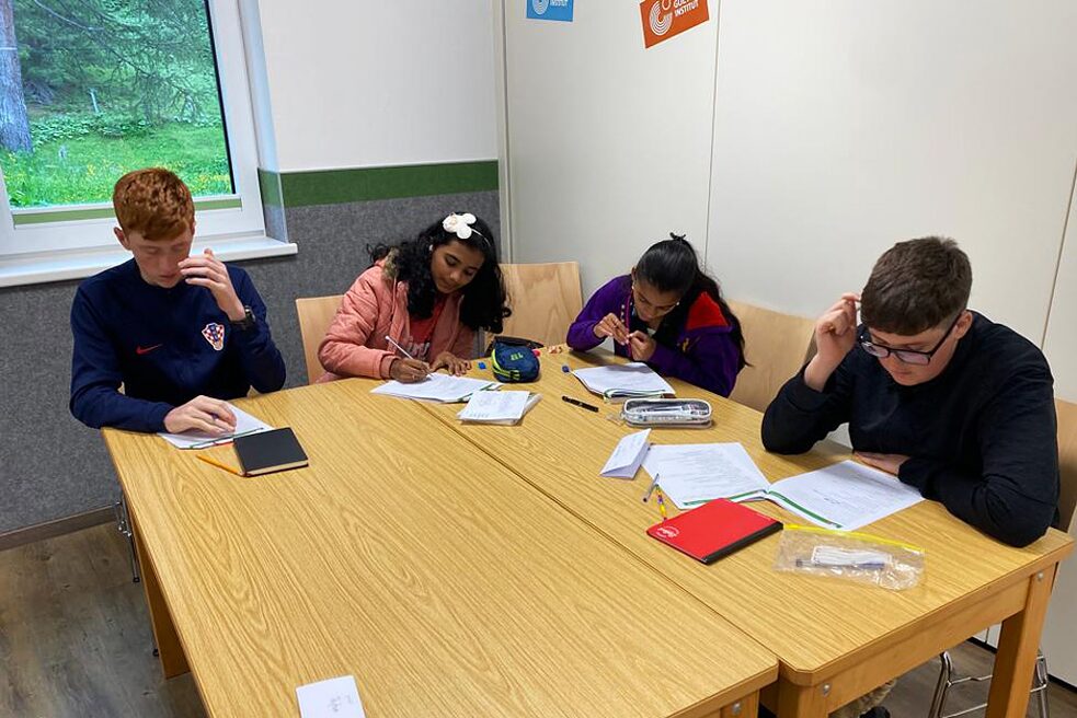 Jugendliche sitzen an einem Tisch und schreiben.