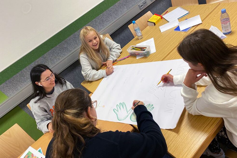 Jugendliche sitzen an einem Tisch und malen. Sie haben sichtlich Spaß.