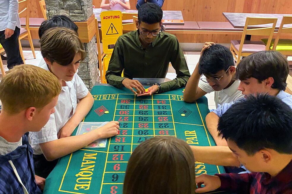 Jugendliche sitzen um einen Roulettetisch herum. 