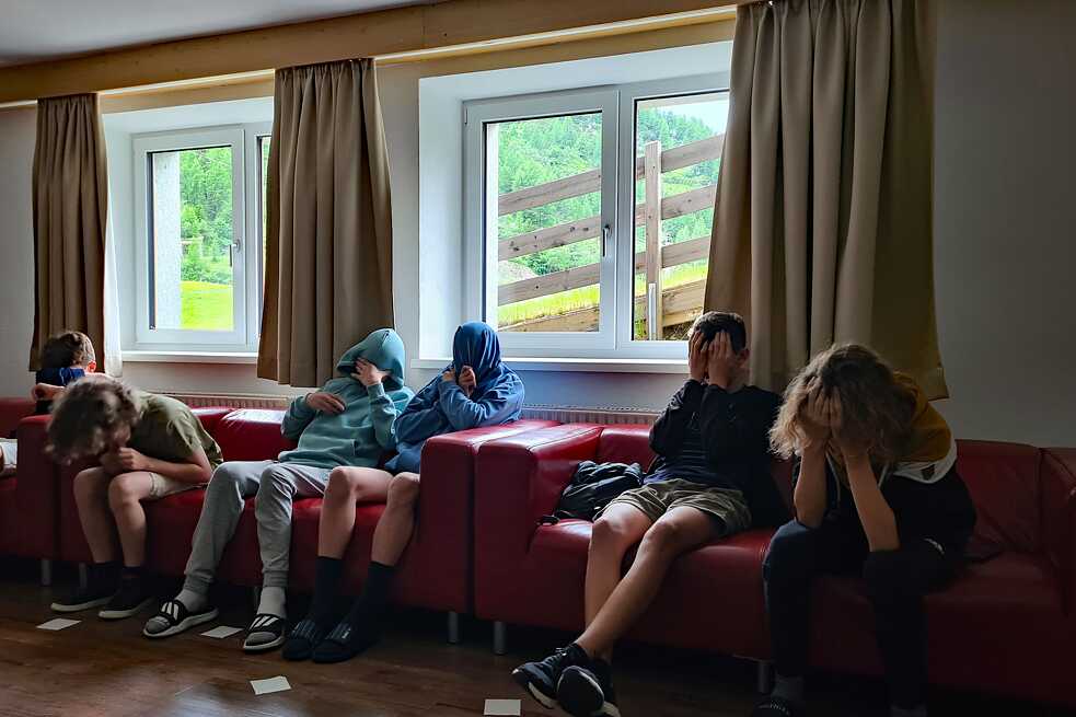Jugendliche sitzen auf einer Couch und halten Ihre Gesichter bedeckt.