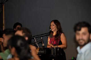 The musician Maschall Ander smiles. In front of her, blurred dancing people can be seen.