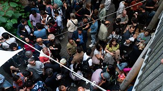 A crowd of people can be seen from above. Most of them are talking to each other in small groups.