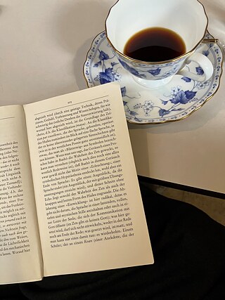Geöffnetes Buch, daneben eine Tasse mit Kaffee