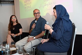 Marina Mohammadi, Ibrahim Hotak and Naeema Ghani sit next to each other. Naeema Ghani speaks, Mr Hotak listens to her with a smile.