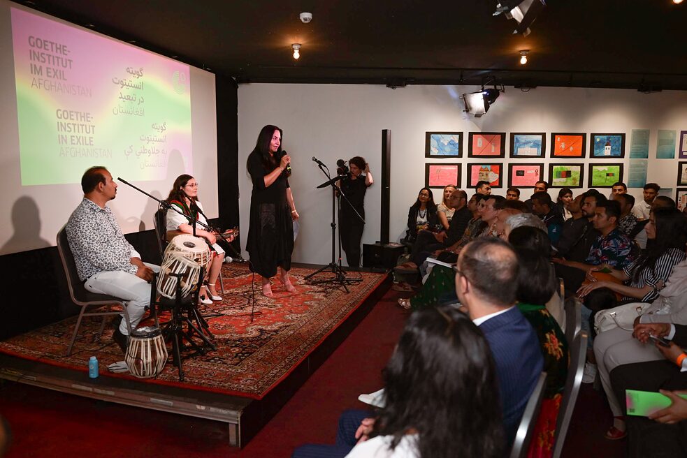 Die Fernseh- und Radiojournalistin Sohayla Asghary steht auf einem Podest und spricht zum Publikum, das rechts vor ihr zu sehen ist. 