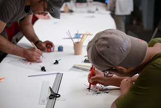 Two people draw and write on a large sheet of paper. 