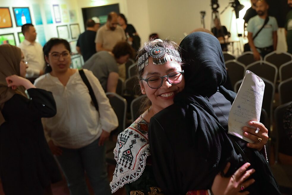 Two women embrace each other. Facing the camera is the journalist Zainab Farahmand.
