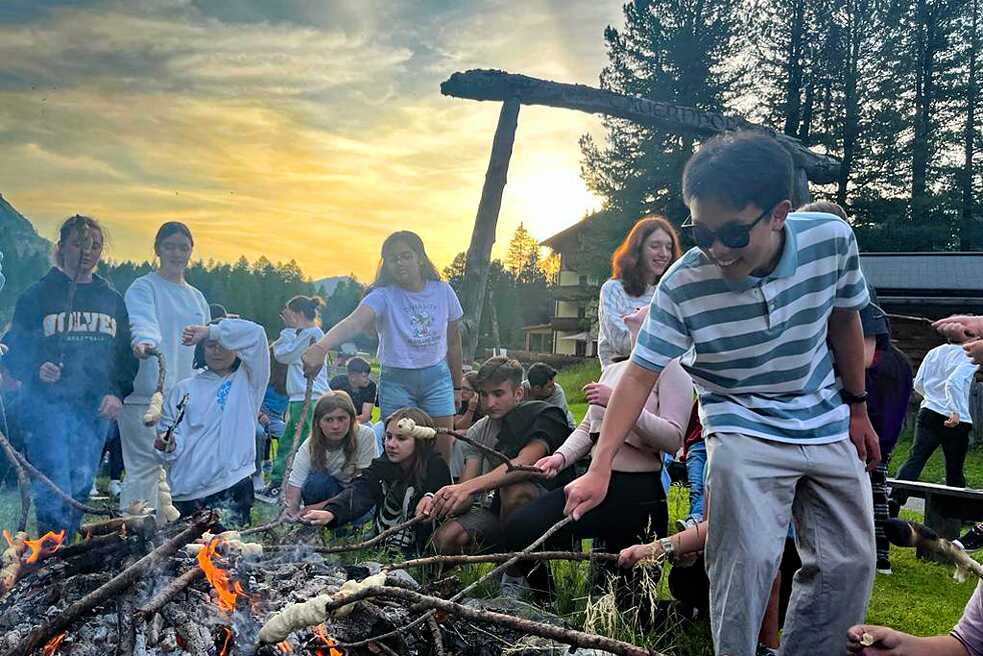 Eine Gruppe Jugendlicher an einem offenen Feuer backen Stockbrot.