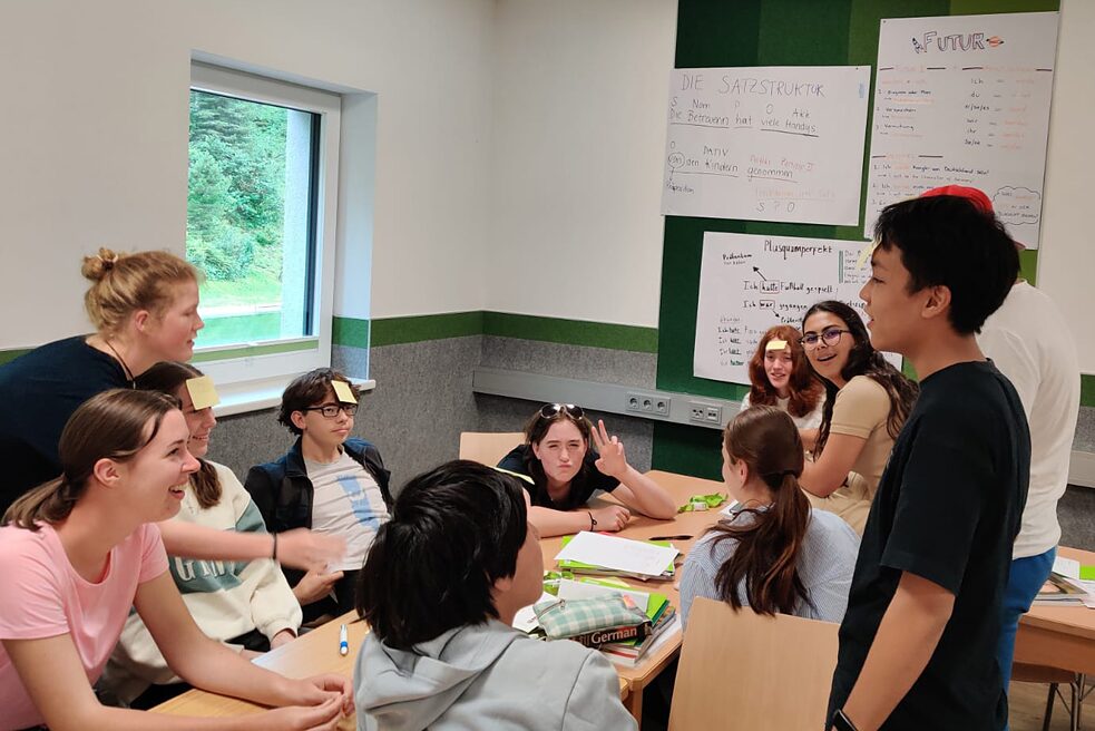 Jugendliche in einem Klassenraum. Sie haben gelbe Post-It an der Stirn.