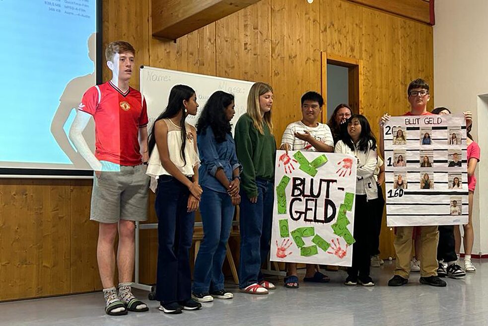 Jugendliche stehen nebeneinander, links eine Projektion. Zwei halten Plakate.